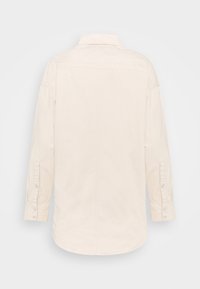 Camicia a maniche lunghe beige chiaro con colletto a bottoni, polsini con singolo bottone e orlo curvo, realizzata in un tessuto liscio e testurizzato.