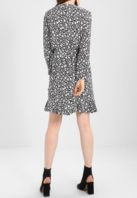 Vestido floral en blanco y negro, con mangas largas, cintura ajustada, dobladillo con volantes y bolsillos laterales. Llevado con tacones negros de punta abierta.