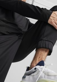 Sort sportslangærmet top og joggebukser med elastiske manchetter, parret med hvide og marineblå sportsko med et gennemsigtigt panel.