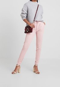 Ljusrosa joggerbyxor i kombination med en grå ribbad tröja, accentuerad med en röd handväska och sandaler med guldklack.