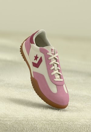 Zapatillas para hombre que presentan una parte superior principalmente blanca con acentos de ante rosa y un logo de estrella roja, complementadas por una suela de goma marrón texturizada.