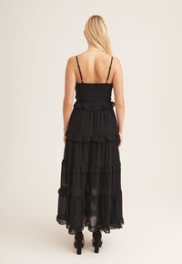 Black maxi dress with layered ruffle design, spaghetti straps, and a fitted bodice. Fabric appears lightweight and slightly sheer at the bottom.