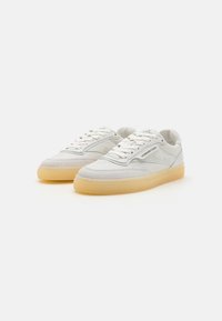 Hvite sneakers med semsket skinn og lær, med et teksturert design, rund tå og en gummisåle. Snøring og logo detaljer er til stede.