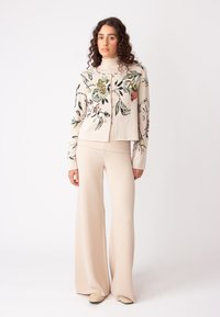 Gebreide cardigan in lichtbeige met bloemmotieven, gecombineerd met crèmekleurige wijde broek. Beschikt over geribbelde manchetten en kraagdetails.
