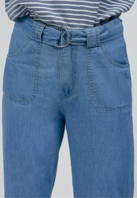 Pantalones de mezclilla azul claro de pierna ancha con un cinturón de hebilla redonda plateada, con dos bolsillos delanteros y detalles de costuras visibles.