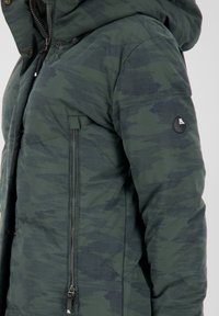 Grön kamoflagepuffjacka med huva. Har en dragkedjefick på sidan och en svart logotypklistermärke på ärmen. Texturerad tygdesign.