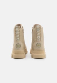 Botas de tornozelo bege com uma textura de couro liso, apresentando um fecho de zíper e um detalhe com o logótipo no calcanhar. Sola de borracha elevada.
