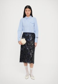Camicia azzurro chiaro a righe con taschino sul petto, abbinata a una gonna midi decorata con paillettes scure. Include calzini bianchi e tacchi color crema.