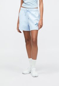 Ανοιχτό μπλε βαμβακερό αθλητικό σορτς με ελαστική μέση, κορδόνι και αντίθετο μπλε λογότυπο. Συνδυάζεται με λευκές κάλτσες και παπούτσια.