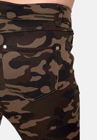 Tarnhosen in grünen, braunen und schwarzen Farbtönen. Verfügt über eine Gesäßtasche mit Nähdetails und metallischen Nieten. Dehnbares Material.