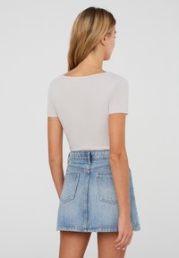 Top corto grigio chiaro a maniche corte con scollatura a barca, abbinato a una mini gonna in denim a vita alta in un lavaggio blu sbiadito.