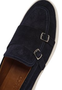 Mocassino in suede di colore blu scuro, suola bianca, chiusura con doppia fibbia e cuciture blu a contrasto lungo i bordi.