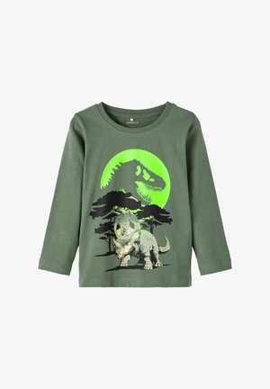 T-shirt à manches longues en coton de couleur verte avec un graphique de dinosaure contre une grande lune verte et des arbres noirs.