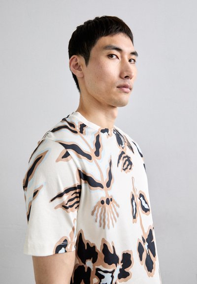 Kortærmet t-shirt i creme med abstrakte sorte, brune og blå blomster mønstre; blødt bomulds-materiale og minimalistisk rund halsudskæring.