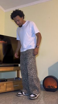 White t-shirt, leopard print loose-fitting pants, black and white sneakers, standing near a TV, wooden media console, and an electric heater.