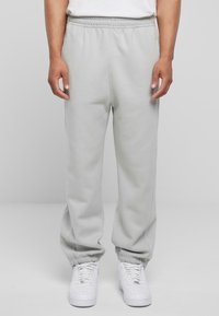 Helle graue Jogginghose mit elastischem Bund und Bündchen an den Knöcheln, aus einem weichen Material; getragen mit weißen Sneakers.