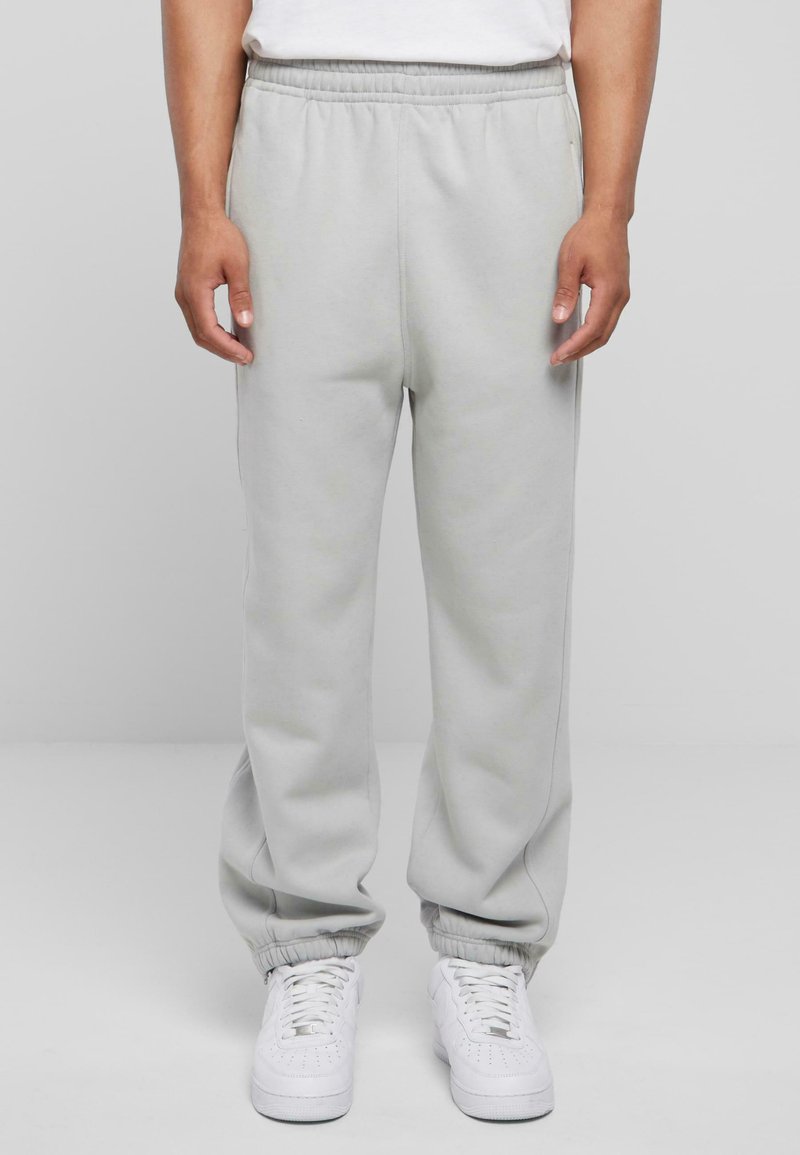 Helle graue Jogginghose mit elastischem Bund und Bündchen an den Knöcheln, aus einem weichen Material; getragen mit weißen Sneakers.