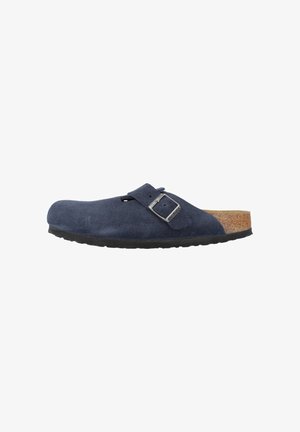 Zoccoli in suede blu navy con soletta in sughero, aperti sul retro e con cinturino regolabile dotato di fibbia metallica. Suola in gomma per garantire aderenza.