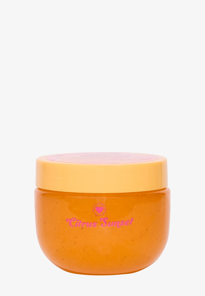 Oransje kroppsskrubb i en rund, gjennomsiktig krukke med en gul lokk. Har rosa "Citrus Sunset" tekst på etiketten. Glatt tekstur.