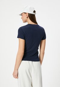 Mørkeblå kortærmet T-shirt i blødt stof, tætsiddende design med rund halsudskæring. Modellen bærer en hvid kasket og lyse bukser.