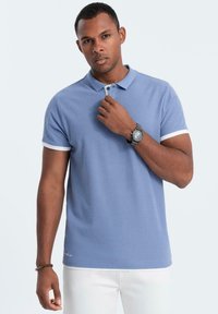 Světle modrá polokošile s krátkým rukávem, bílými lemy a límečkem. Hladká tkanina s přiléhavým střihem. Nosit s bílými kalhotami a hodinkami.