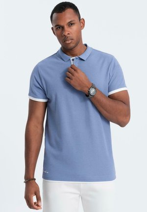  Lichtblauwe polo met korte mouwen, witte randen en een kraag. Gladde stof met een fitted ontwerp. Draag met witte broek en een horloge.