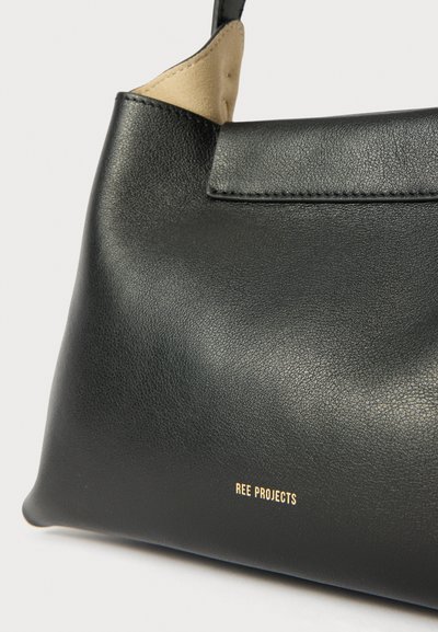 Sac en cuir noir avec une texture lisse, arborant un logo doré et une doublure intérieure beige contrastante. Design minimaliste avec une silhouette élégante.