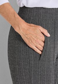 Zwart-wit houndstooth-gepatenteerde broek met een zijzak en een hoge tailleband, met een hand die casual in de zak rust.