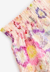 Blommönstrad tyg i nyanser av rosa, lila och gult, med en insydd midjedetalj och en slät, texturerad yta.