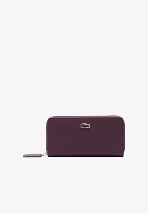 Cartera rectangular morada con cierre de cremallera alrededor, superficie texturizada, logo de cocodrilo plateado centrado y tirador de cremallera morado a juego.