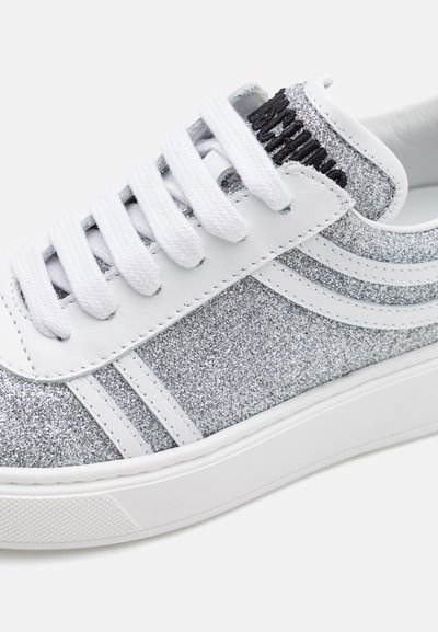 Zapatillas brillantes plateadas con acentos de cuero blanco, que presentan cordones blancos, rayas dobles en los laterales y una suela de goma texturizada.