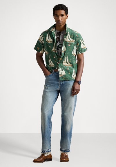 Korte mouwen groene shirt met een nautisch zeilbootpatroon, gecombineerd met lichtblauwe spijkerbroek en een paar bruine leren schoenen.