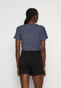 Kuttet marineblå topp med diamantmønster, korte ermer og teksturert stoff, sammen med svarte vide shorts.