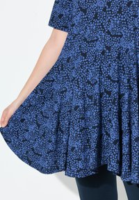Sininen lyhythihainen mekko, jossa on liehuva muotoilu, tummansininen pohja ja vaaleansininen pilkkukuvio. Pehmeä kangas, jossa on virtaava tekstuuri.