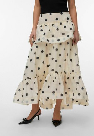 Lag på lag beige nederdel med store sorte polkaprikker, båret med sorte spidse slingback-hæle og en sort ærmeløs top.