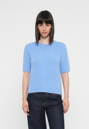 Lyseblå kortermet genser laget av mykt, fluffy materiale med rund halslinning og ribbestrikket nederkant, kombinert med mørkejeans.