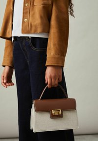 Pruun nahast käekott halli tekstuuritud kangast kerega, ristkülikukujuline ja kuldse riistvaraga klambri peal. Käes hoitud, kombineeritud teksadega.