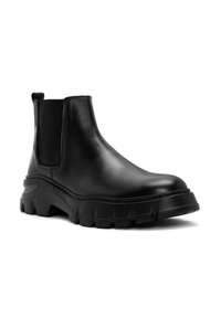 Las botas negras de cuero hasta el tobillo cuentan con una suela gruesa y estriada, así como paneles laterales elásticos. El diseño es elegante, con un acabado suave y una lengüeta.