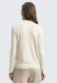 Pulover crem cu nervuri, cu mâneci lungi, material texturat și guler rotund, purtat cu pantaloni de culoare deschisă. Privirea din spate arată o croială relaxată.
