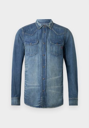 Džínová košeľa, svetlomodrá, s dlhými rukávmi, s kravátkovým zapínaním vpredu, s dvoma náprsné vreckami, západný strih a akcenty prešívania, so známkami opotrebovania.