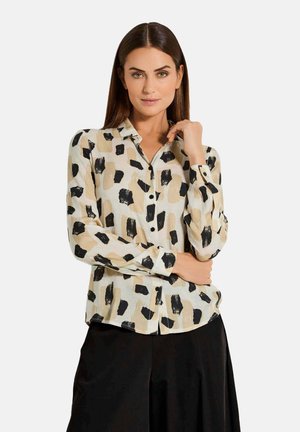 Das Button-Up-Hemd hat eine cremefarbene Basis mit großen, schwarzen und beigen Pinselstrichmustern. Es verfügt über lange Ärmel und einen klassischen Kragen.