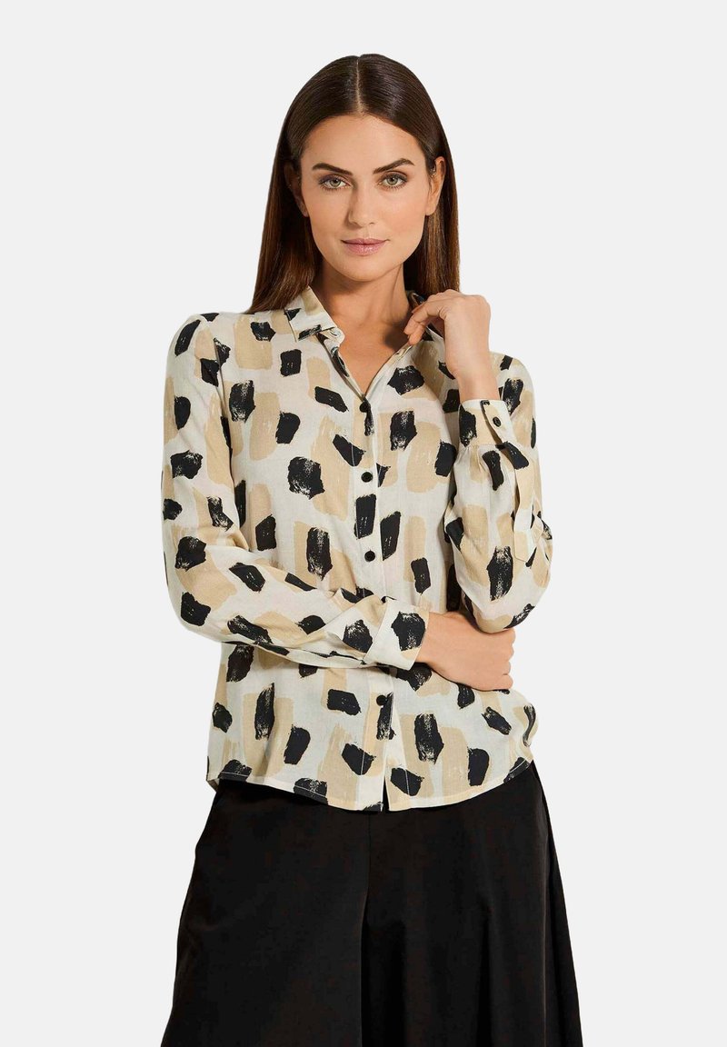 Das Button-Up-Hemd hat eine cremefarbene Basis mit großen, schwarzen und beigen Pinselstrichmustern. Es verfügt über lange Ärmel und einen klassischen Kragen.
