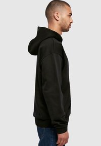 Felpa con cappuccio nera in vestibilità rilassata. Caratterizzata da un tessuto morbido, polsini a costine e una tasca a marsupio. Design semplice senza motivi.
