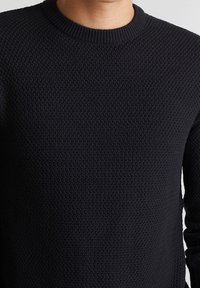 Maglione nero lavorato a maglia con un motivo testurizzato in rilievo e scollatura rotonda, dotato di maniche lunghe e un design aderente.