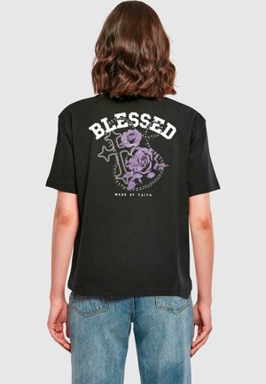 T-shirt noir avec le texte blanc "BÉNI" et un design de roses violettes avec une croix. Manches courtes, coupe standard, en coton.