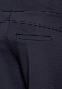 Navy fabric pants with a smooth texture, featuring a back pocket with an inset design, visible stitching, and a tailored fit.