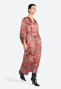 Il modello si erge con sicurezza indossando un vestito floreale fluido con maniche lunghe, abbinato a stivali neri alla coscia alla moda.