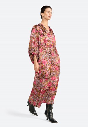 Model staat zelfverzekerd in een luchtige, bloemenpatroon jurk met lange mouwen, gecombineerd met stijlvolle zwarte kniehooglaarzen.