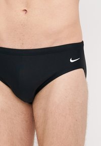 Mustat uimapossut, jotka on valmistettu joustavasta kankaasta. Edessä vasemmalla puolella on valkoinen Nike-logo, ja ne ovat yksinkertaiset ja istuvat hyvin.