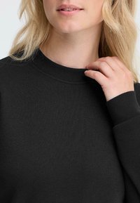 Felpa nera con un collo rotondo e polsini a costine, realizzata in un morbido tessuto testurizzato. La vestibilità sembra morbida e informale.